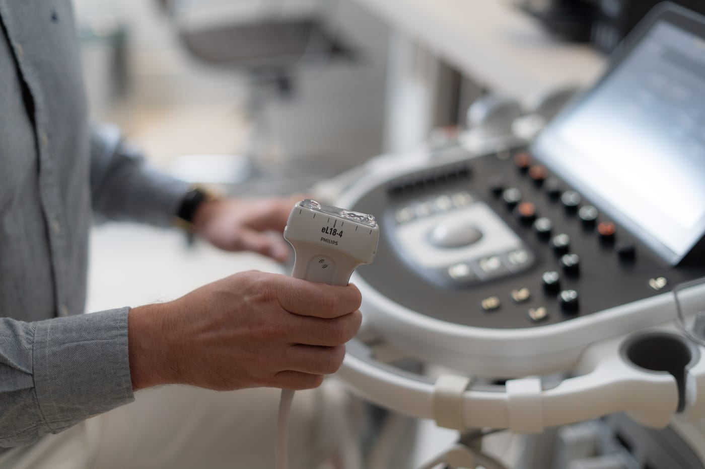 Mão segurando o transdutor do aparelho de ultrassom no consultório, durante a avaliação do joelho